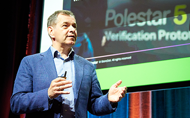 A speaker engage the audience on stage at a bustling show floor, sharing insights and expertise.